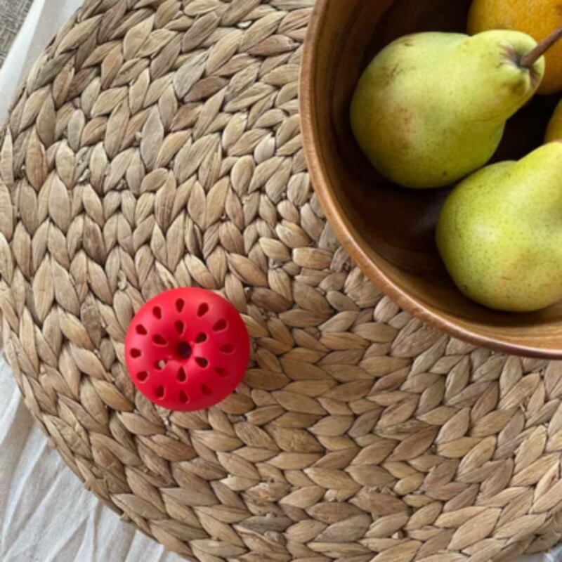Red apple-shaped fruit fly trap next to a bowl of pears